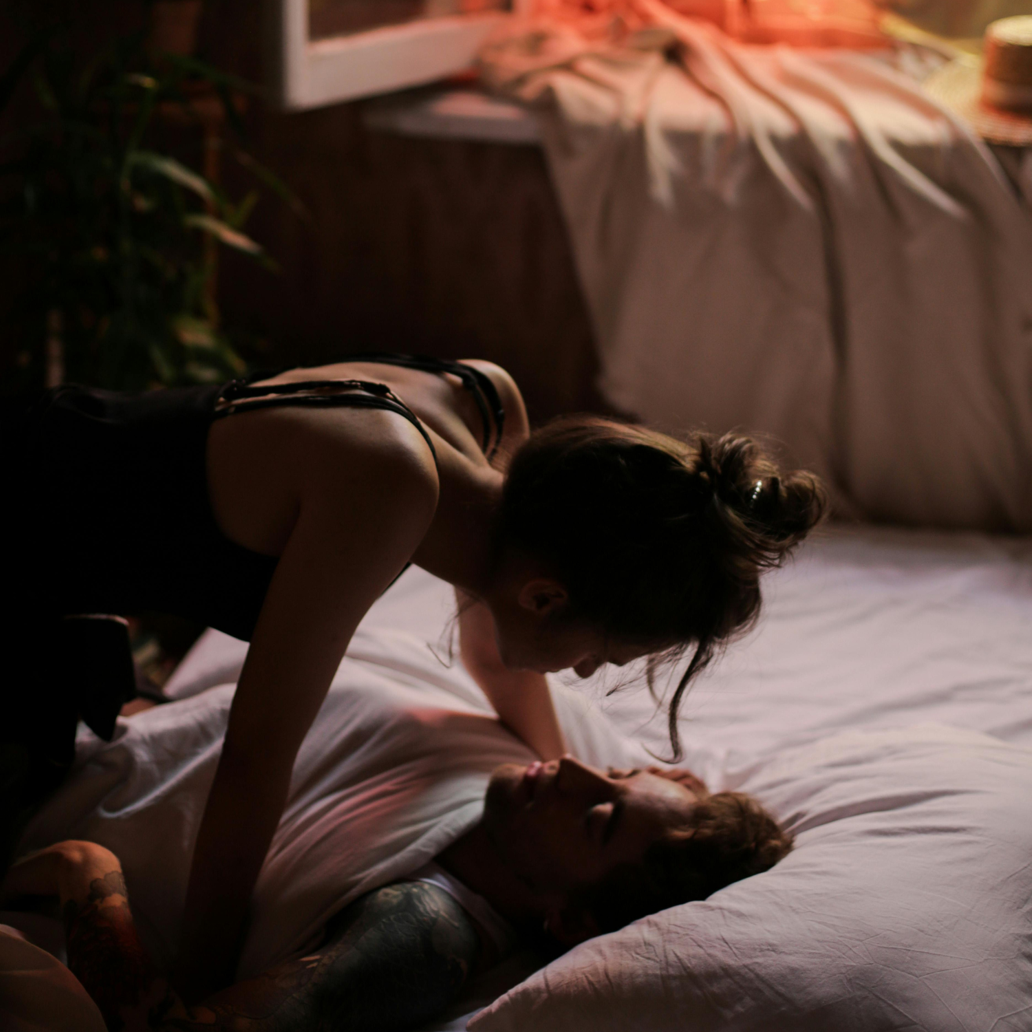 Photo d'un couple couché dans des draps blancs devant une fenêtre ouverte dans un contexte coquin spicy érotique et moody
